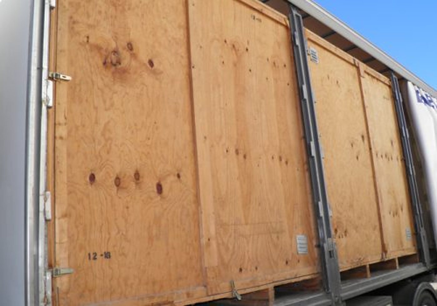 Des grandes caisses en contreplaqué sont alignées à l'intérieur d'une remorque ouverte, prêtes pour un transport ou un déménagement.
