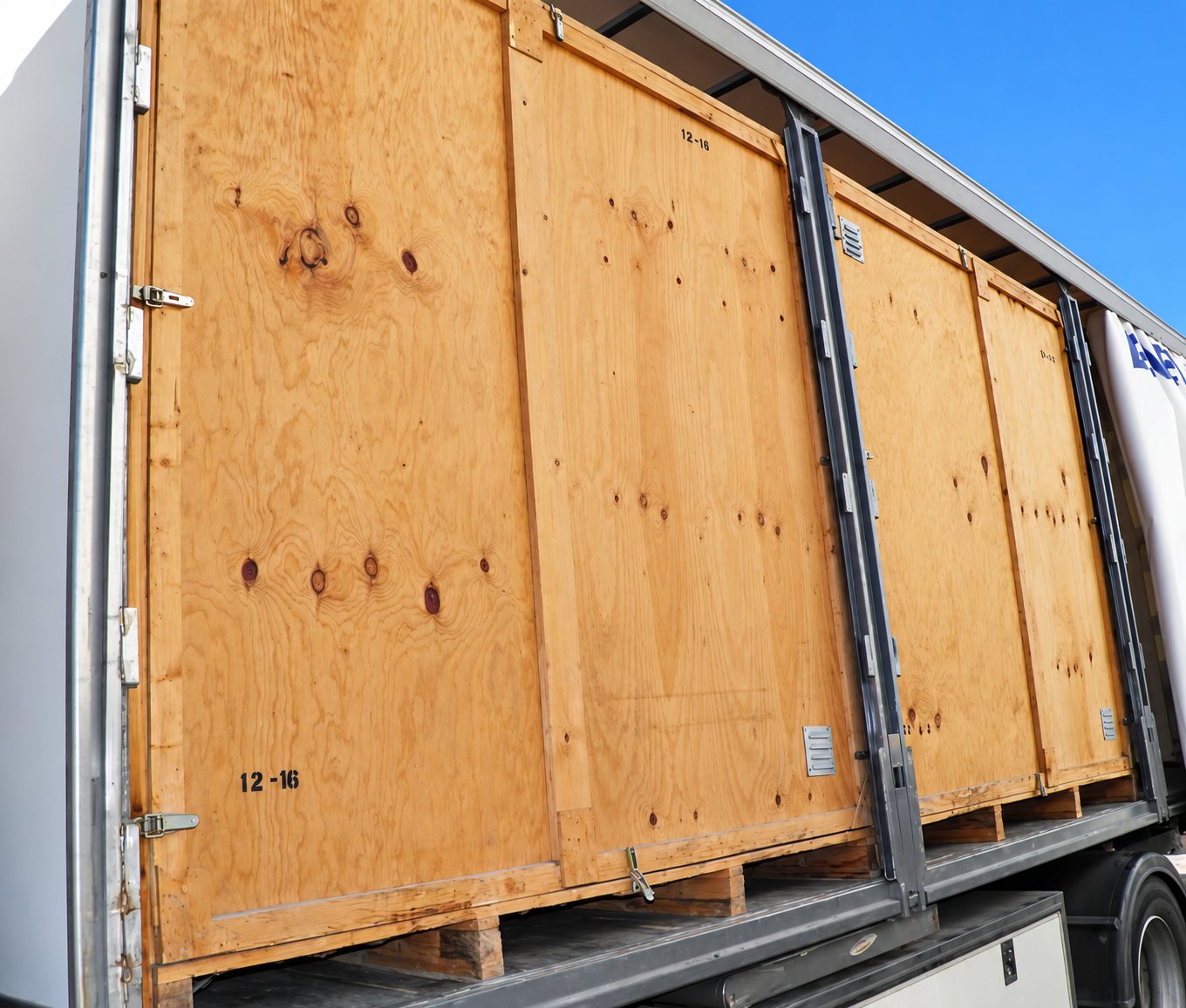Grandes caisses en contreplaqué posées sur des palettes à l'intérieur d'une remorque de camion à rideaux coulissants.